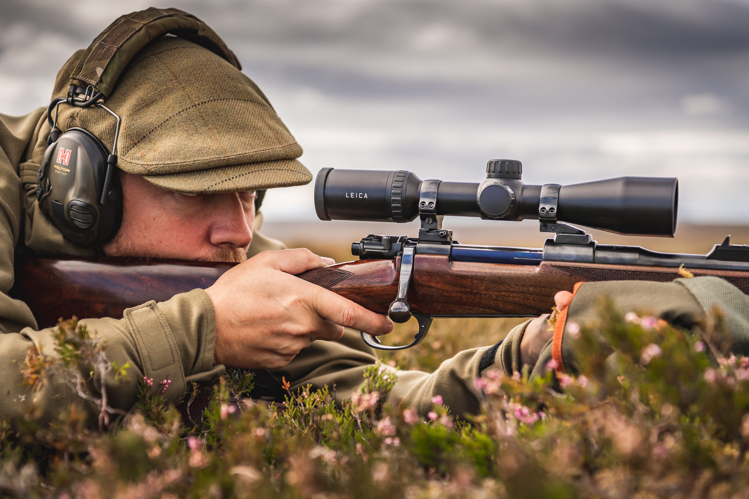 Man laying in heather looking through a rifle scope