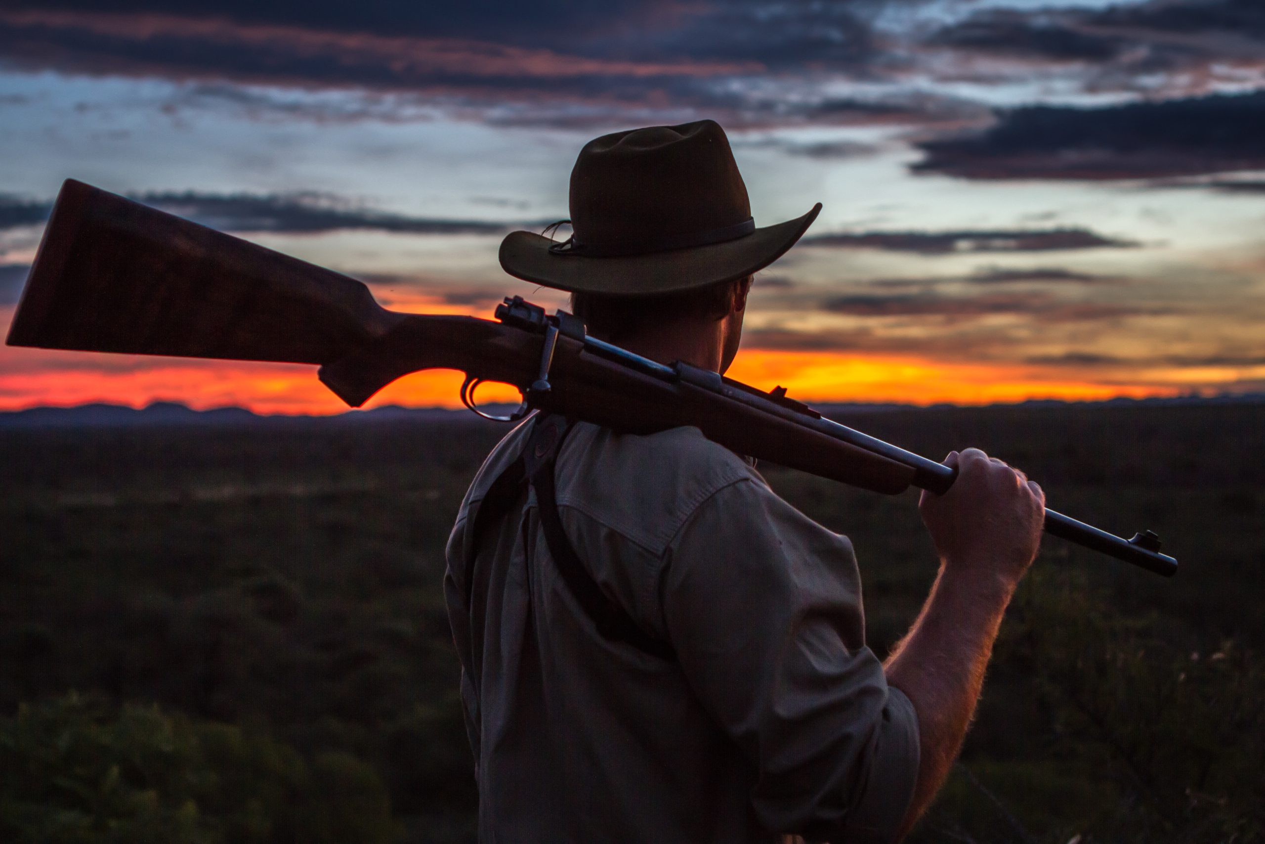 Man looking at the sunset with a rifle over his shoulder