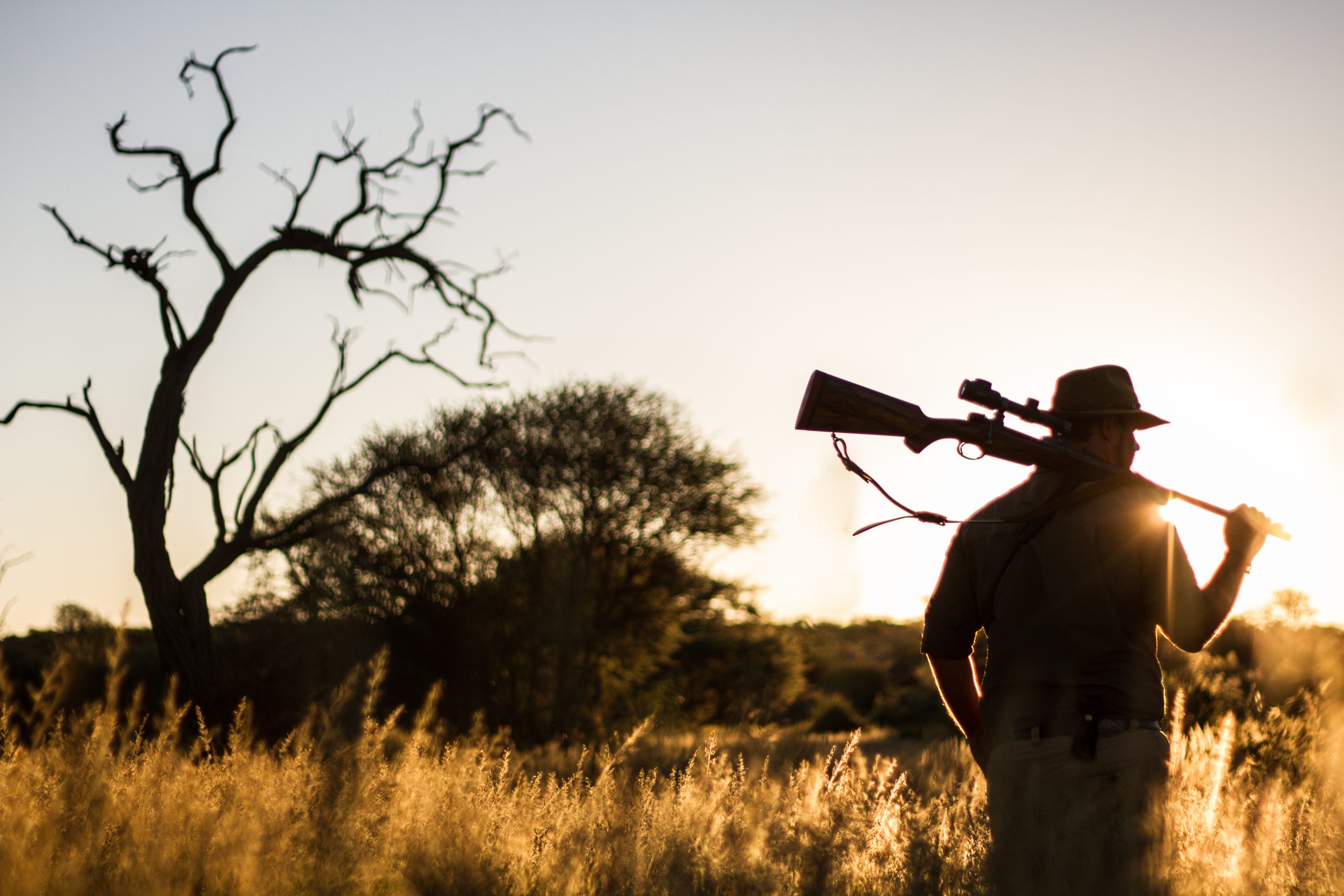 Man walking into the sunset with a rifle over his shoulder