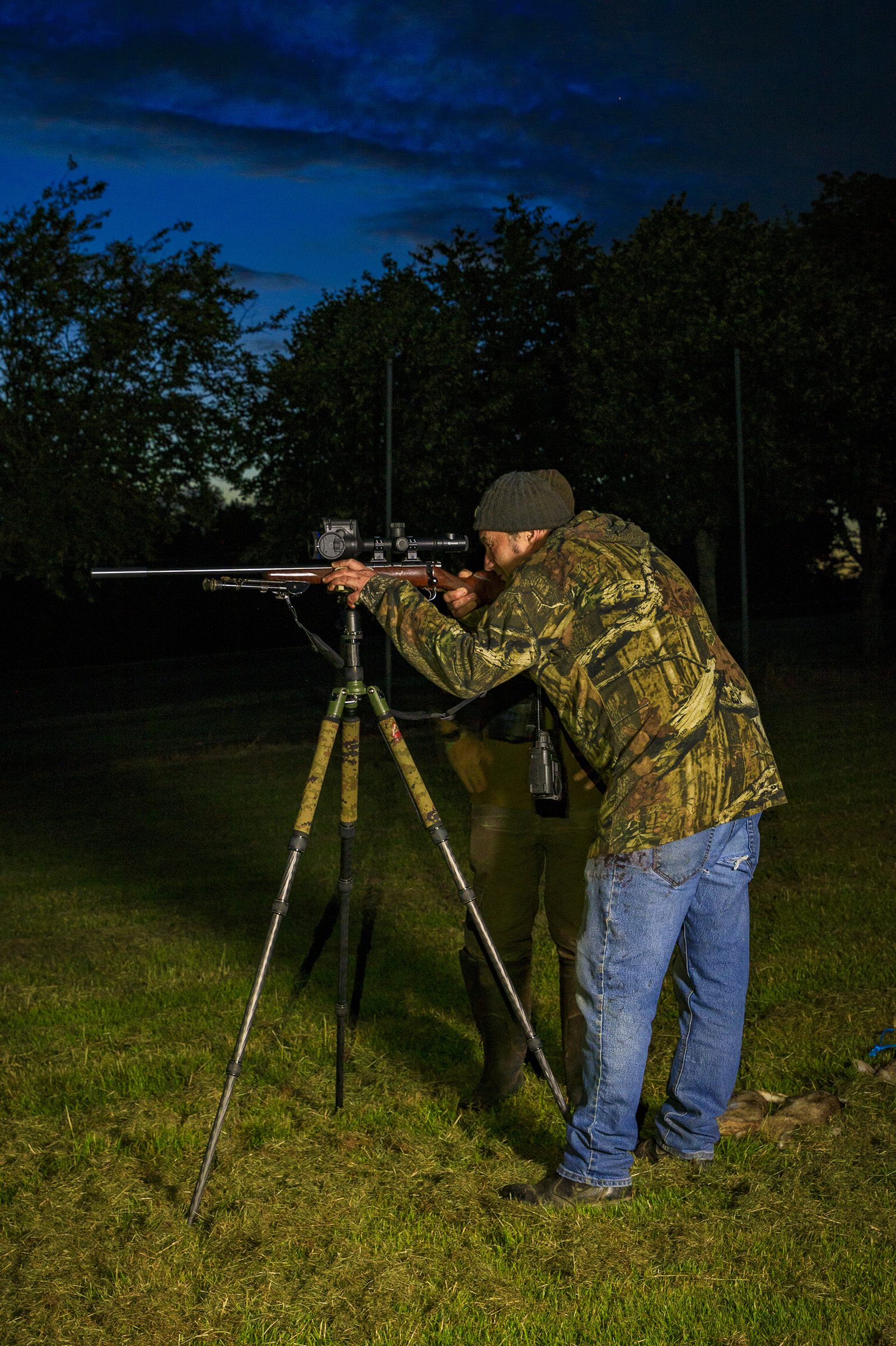Shooter aiming a .22LR rabbiting rifle from a tripod during night rabbit control